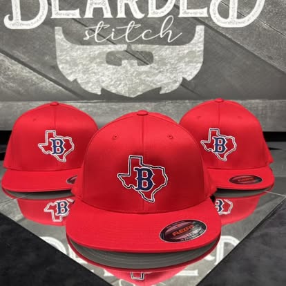 Red custom team caps with an embroidered B Texas logo displayed at Bearded Stitch